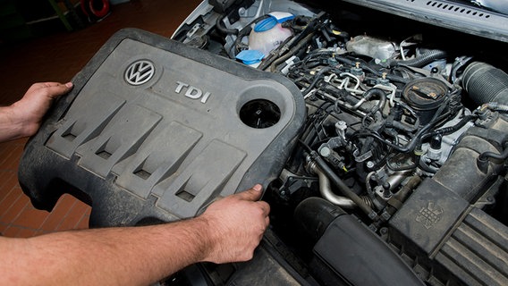 Ein KFZ-Servicetechniker hält die Abdeckung vor einem vom Abgas-Skandal betroffenen 2.0l TDI Dieselmotor vom Typ EA189 in einem VW Touran in einer Autowerkstatt in Hannover (Niedersachsen). © dpa-Bildfunk Foto: Julian Stratenschulte