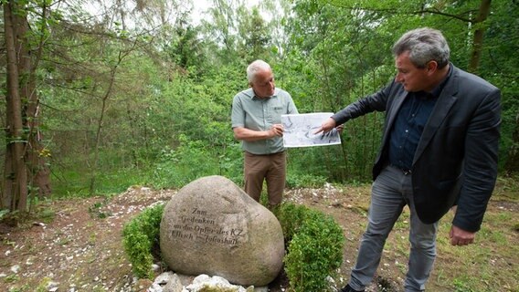 Jens-Christian Wagner (r.), Geschäftsführer der Stiftung niedersächsische Gedenkstätten, und Henning Haßmann, Landesarchäologe vom niedersächsischen Landesamt für Denkmalpflege, stehen mit einer hochauflösende Abbildung der Geländeoberfläche neben einem Gedenkstein vor dem Fundort des Sammelgrabes. © dpa-Bildfunk Foto: Swen Pförtner