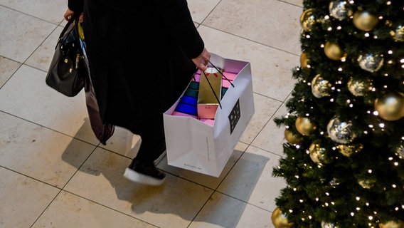 Eine Person trägt eine Tüte mit Einkäufen, daneben ein Weihnachtsbaum © dpa-Bildfunk 