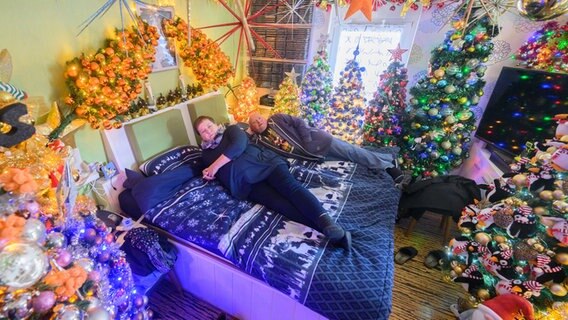 Susanne und Thomas Jeromin liegen auf ihrem Bett inmitten von Weihnachtsbäumen in ihrem Haus im Landkreis Schaumburg. © dpa-Bildfunk Foto: Julian Stratenschulte