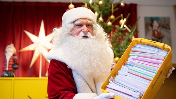 Ein als Weihnachtsmann verkleideter Mann hält eine Kiste mit Briefen in den Händen. © picture alliance/Soeren Stache/dpa-Zentralbild/dpa Foto: Soeren Stache