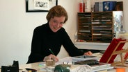 Isabel Kreitz sitzt an einem Schreibtisch mit einem Zeichenstift in der Hand. © privat 
