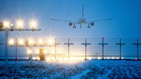Ein Flugzeug landet bei leichten Schneefall in der Abendddämmerung. © dpa Foto: Julian Stratenschulte