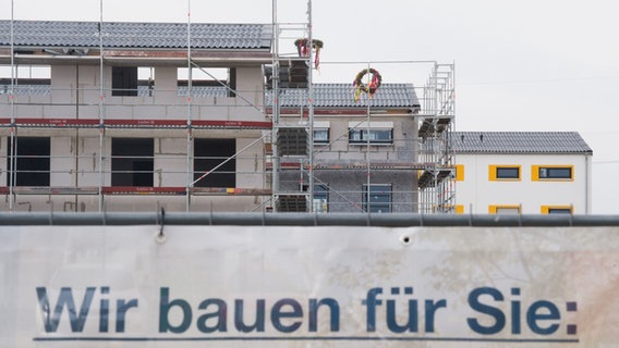 Ein Bauzaun mit der Aufschrift: "Wir bauen für Sie" steht vor einem Neubau mit Baugerüst. © dpa-Bildfunk Foto: Julian Stratenschulte