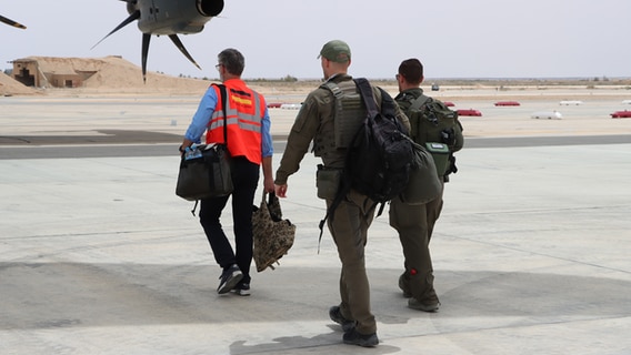 Three men walk to a German army transport plane at Al-Asaq Air Force Base.  © Bundeswehr Photo: Hultgren