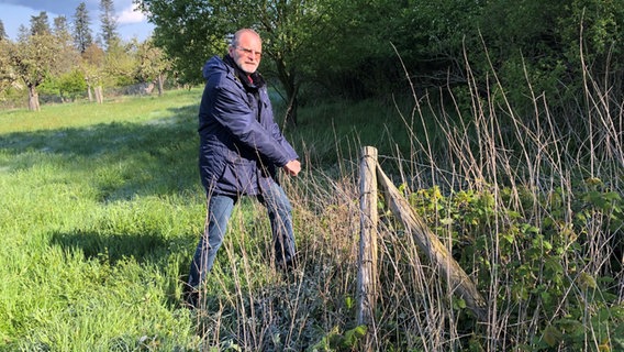 Ein Mann zeigt auf einen alter Zaun auf einer Wiese. © NDR Foto: Wilhelm Purk