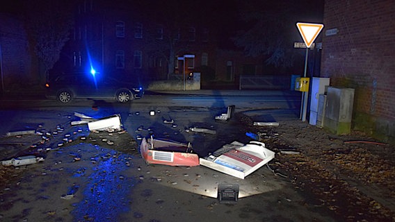 Mehrere Teile eines gesprengten Zigarettenautomaten liegen auf dem Boden. Dahinter ein Auto mit Blaulicht. © Polizeiinspektion Hameln-Pyrmont/Holzminden 