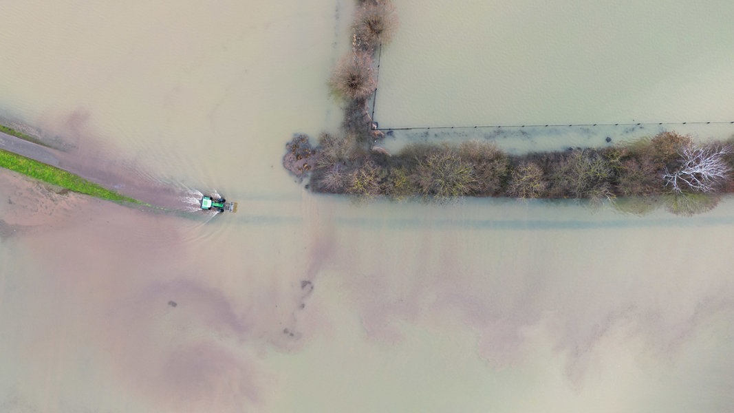 Ein Traktor fährt auf einem Feldweg zwischen überfluteten Feldern