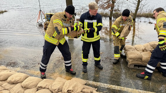 Einsatzkräfte der Feuerwehr stapeln Sandsäcke in Hodenhagen. © NDR Foto: Benedikt Bathe
