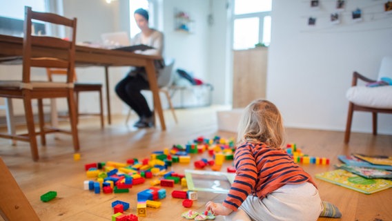 Ein Kind spielt auf dem Küchenboden, während die Mutter im Homeoffice arbeitet. © dpa-Bildfunk Foto: Julian Stratenschulte