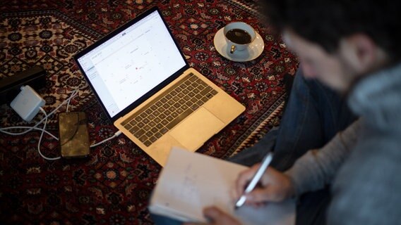 Ein Mann sitzt im Homeoffice mit Laptop auf dem Teppich und arbeitet. © picture alliance/dpa Foto: Sina Schuldt