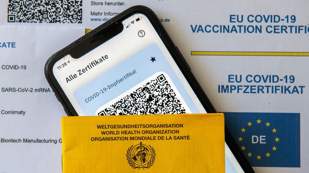 Ein Impfpass und ein Smartphone, auf dem die App CovPass läuft, liegen auf einem Impfzertifikat.