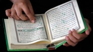 Hände halten einen aufgeschlagenen Koran.  Foto: Epa / Ali Ali
