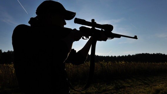 Eine Jägerin steht mit ihrem Gewehr in einem Waldstück. © dpa Foto: Philipp Schulze