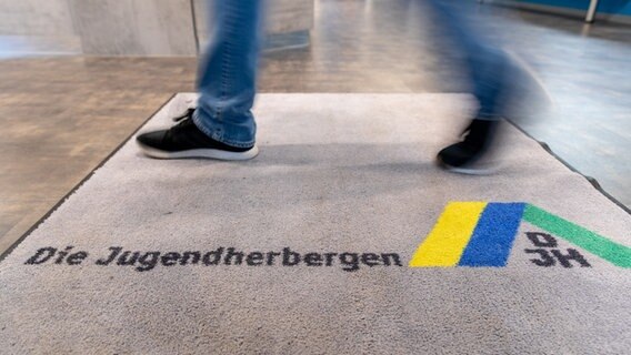 Ein Mann läuft über einen Teppich im Eingang einer Jugendherberge. © picture alliance/dpa/Friso Gentsch Foto: Friso Gentsch