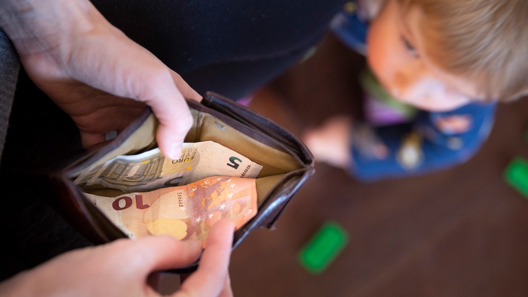 Eine Mutter schaut in eine Geldbörse, während ein Kind vor ihr steht.