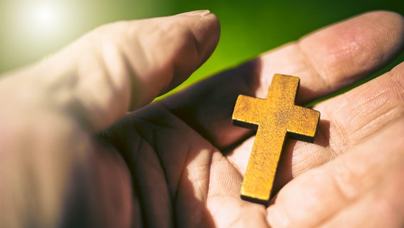 Eine Hand hält ein Holzkreuz. Eine Hand hält ein Holzkreuz. © picture alliance/CHROMORANGE/Christian Ohde Foto: Christian Ohde