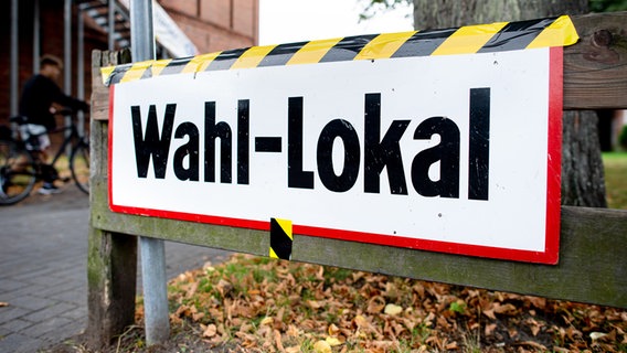 Ein Schild mit der Aufschrift "Wahl-Lokal" hängt an der Zufahrt zu einer Grundschule, in der ein Wahllokal für die Kommunalwahl untergebracht ist. © picture alliance/dpa/Hauke-Christian Dittrich Foto: Hauke-Christian Dittrich