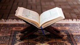 Ein geöffneter Koran steht auf einem Gebetsteppich.