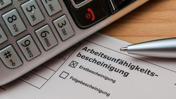 Eine Bescheinigung der Arbeitsunfähigkeit und ein Telefon © picture alliance/Zoonar | stockfotos-mg 