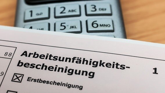 Eine Arbeitsunfähigkeitsbescheinigung liegt neben einem Telefon. © picture alliance / Zoonar | stockfotos-mg 