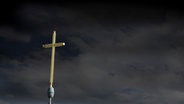 Ein Kreuz vor einem wolkenverhangenen Himmel. © picture alliance 