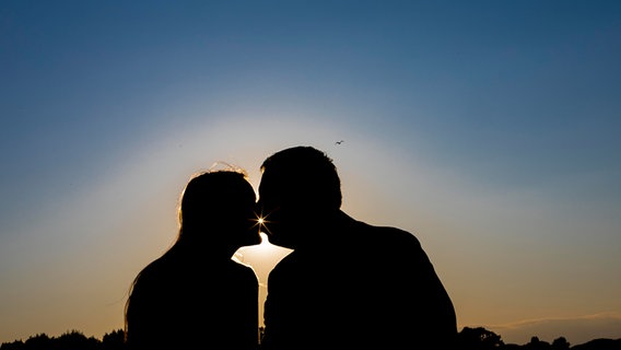 Die Silhouetten einer frau und eines Mannes, die sich im Sonnenuntergang küssen. © picture alliance Foto: imageBROKER | Andrea Matone