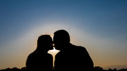 Die Silhouetten einer frau und eines Mannes, die sich im Sonnenuntergang küssen. © picture alliance Foto: imageBROKER | Andrea Matone