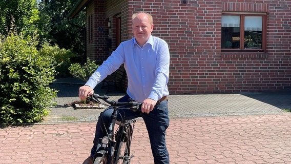 Minister Hilbers (CDU) sitzt vor einem Wohnhaus auf einem Fahrrad. © Niedersächsisches Finanzministerium 