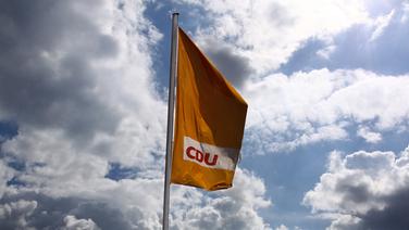 Eine Fahne der CDU weht vor bewölktem Himmel. © dpa picture alliance 