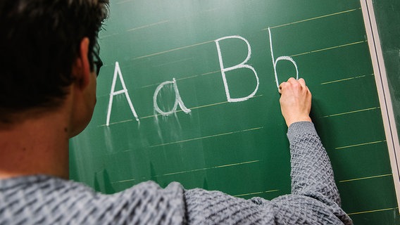 Ein Lehrer schreibt Buchstaben an eine grüne Tafel. © NDR Foto: Julius Matuschik