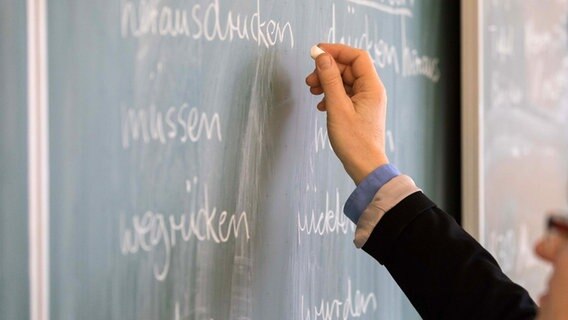 Die Hand einer Lehrerin schreibt mit Kreide etwas an eine Tafel. © dpa - Bildfunk Foto: Mohssen Assanimoghaddam
