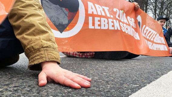 Ein Aktivist der Gruppe Letzte Generation hat seine Hand auf einer Straße festgeklebt. © NDR Foto: Johannes Koch