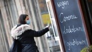 Eine Frau steht vor einem Laden, vor dem eine Tafel steht mit der Aufschrift: "Wegen Corona Lockdown geschlossen." © picture alliance Foto: SvenSimon