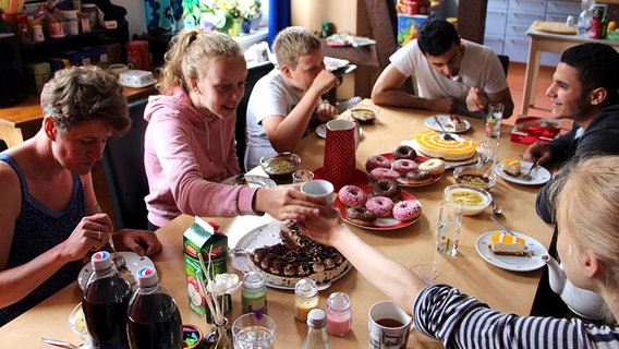 Mohammad und Abdullah Abd sitzen gemeinsam mit Familie Berndt am Tisch und essen Kuchen. © NDR Foto: Christian Berndt
