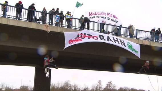Aktivistinnen seilen sich von einer Autobahnbrücke ab und hissen ein Transparent. © NDR 