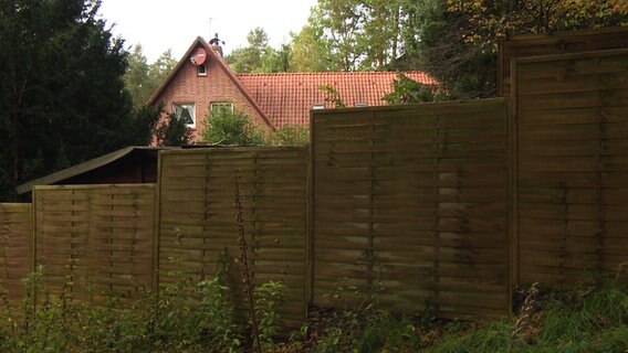 Ein Zaun vor einem Backsteinhaus. © NDR 