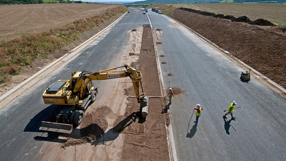 Zwei Bauarbeiter stehen auf einer Autobahnbaustelle zwischen zwei Feldern. ©  picture alliance/dpa-Zentralbild Foto: Robert Michael