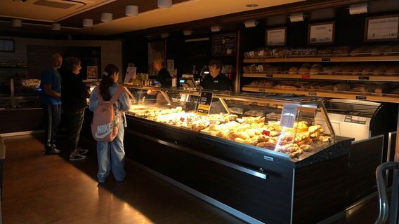 Kunden stehen in einer Bäckereifiliale, in der kaum Licht brennt. © NDR Foto: Göran Theo Ladewig