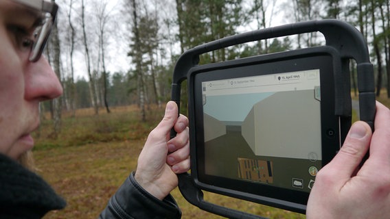 Ein Historiker hält ein iPad hoch und testet das Bergen-Belsen-App. © NDR Foto: Vassili Golod