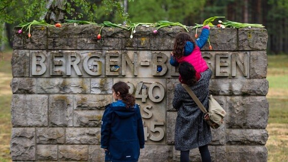 Eine Frau legt mit ihren Kindern Tulpen auf einer Mauer mit der Inschrift "Bergen-Belsen, 1940 bis 1945" ab. © dpa-Bildfunk Foto: Philipp Schulze