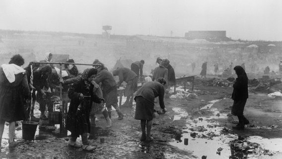 Menschen stehen im Konzentrationslager Bergen-Belsen auf dem Waschplatz. © picture alliance/akg-images 