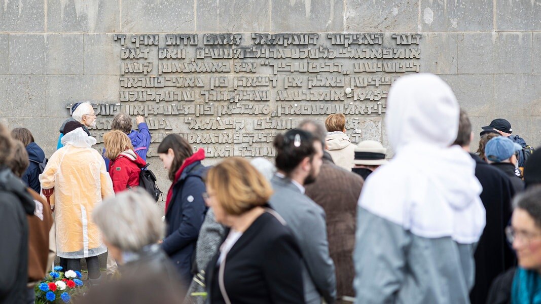 Besucher stehen nach einer Gedenkveranstaltung zum 79. Jahrestag der Befreiung des ehemaligen Konzentrationslagers Bergen-Belsen vor einer Inschriftenwand auf dem Gelände der Gedenkstätte.