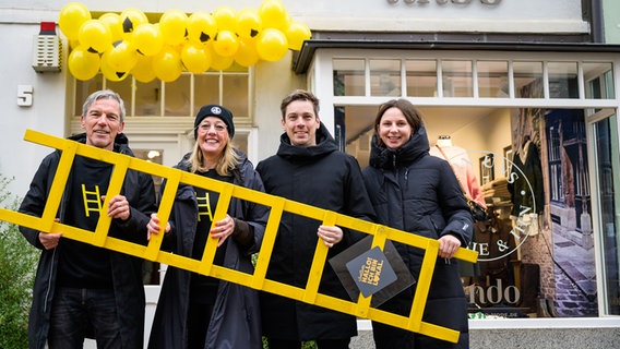 Die Initiatoren von "Best statt Black Friday in Lüneburg" stehen mit einer gelben Leiter vor einem inhabergeführten Geschäft. © picture alliance/dpa | Philipp Schulze Foto: Philipp Schulze