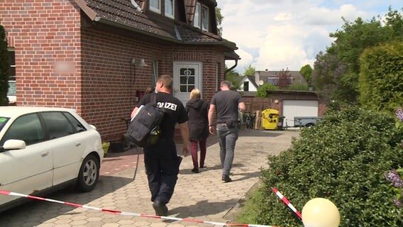 Einsatzkräfte der Polizei laufen auf die Eingangstür eines Einfamilienhauses zu.  