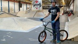 Ein Mann steht mit einem BMX-Rad in einer Halle. In der Halle sind zahlreiche Rampen aufgebaut. © NDR Foto: Alex Lofink