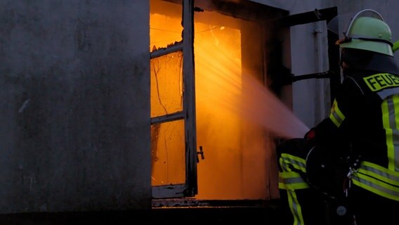 Ein Feuerwehrmann löscht ein Feuer durch ein Fenster. © Feuerwehr Lüchow-Dannenberg 