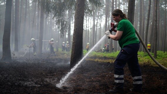Eine Einsatzkraft der Feuerwehr löscht mit einem Schlauch in einem Waldstück. © Philipp Schulze/dpa Foto: Philipp Schulze