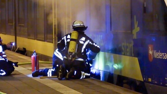 Feuerwehrleute knien auf einem Bahnsteig vor einem qualmenden Zug. © TV-Elbnews 