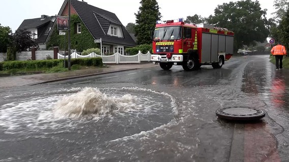 Ein Feuerwehrwagen steht in Buchholz neben einem Gulli, aus dem Wasser sprudelt. © Hellwig TV-Elbnews Produktion 